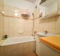 Badezimmer mit Dusche und Waschbecken in einer 2-Zimmer-Wohnung, gefliest mit hellen Fliesen.