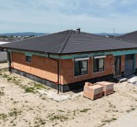 Ein Einfamilienhaus in Bernolákovo mit unverputzten Ziegeln, einem Schrägdach und einem ungepflegten Grundstück.