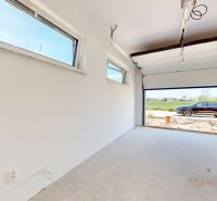 Eine Garage in einem Einfamilienhaus mit offenen Türen, Blick auf ein Auto und Grünflächen.