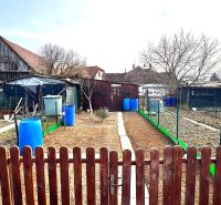 Der Garten in Hlboké mit ländlichen Gebäuden und Fässern zwischen den Zäunen.