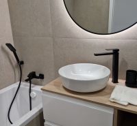 Badezimmer in einer 3-Zimmer-Wohnung mit rundem Spiegel und modernen Armaturen.