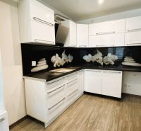 Küche in einer 4-Zimmer-Wohnung mit weißen Möbeln und einem Boden in Holzoptik.