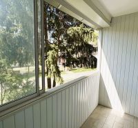 Ein verglaster Balkon in einer 4-Zimmer-Wohnung mit Blick auf Bäume, weiße Holzwand.