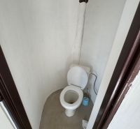Einfache Toilette in einer Hütte mit unverkleideter Wand und Plastik-WC.