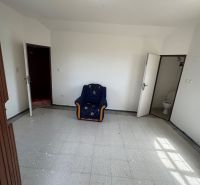 Ein Zimmer mit einem Sessel, weißen Wänden, Fliesenboden und einer Tür, die zu einer Toilette in der Hütte führt.
