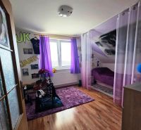 Kinderzimmer mit lila Vorhängen, Teppich, Bett, Boden mit Holzdekor.