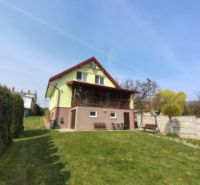 Ein Einfamilienhaus in Klokočov mit einem Rasen-Garten und einer Terrasse auf einem Hanggrundstück.