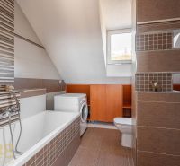 Badezimmer mit Satteldach, Badewanne, Waschmaschine und braunen Fliesen in einer 4-Zimmer-Wohnung.