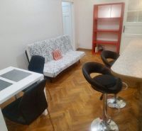 Wohnzimmer einer Zweizimmerwohnung mit Holzboden, Esstisch und Barhockern.
