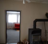 In einem Einfamilienhaus gibt es einen Deckenventilator, einen Kaminofen und ein rotes Sofa im Hintergrund.