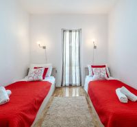 Ferienwohnung mit zwei Betten, roter Decke und Holzboden.