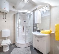 Badezimmer in einer Ferienwohnung mit moderner Duschkabine und leuchtend gelben Handtüchern.