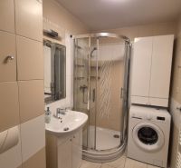 Badezimmer mit Waschbecken, Duschkabine und Waschmaschine in einer Ferienwohnung.