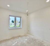 Ein leerer Raum in einem Einfamilienhaus mit weißen Wänden und einem Fenster mit Blick nach draußen.