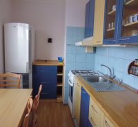 Küchenbereich in einer 2-Zimmer-Wohnung mit Stühlen, Holzboden, blaue Fliesen.