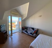Zimmer in einer Ferienwohnung mit Balkon und Meerblick, Fernseher und Sofa.