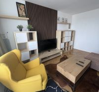 Wohnzimmer mit Holzboden, gelbem Sessel und Couchtisch aus Holz.