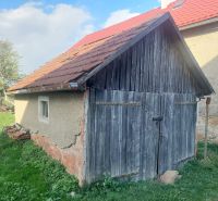 Eine alte Holzhütte auf einem Wohngrundstück in Budiná, umgeben von Grün und Bäumen.