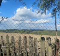 Blick auf Felder und Hügel in Budiná, umgeben von einem Zaun; Grundstücke - Wohnen.