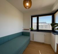 Ein Zimmer mit einem Sofa, Fenstern mit Jalousien und einem Holzboden in einer 2-Zimmer-Wohnung.