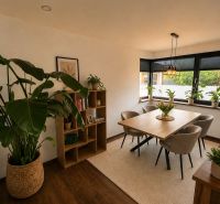 Esszimmer in einem Einfamilienhaus mit Holzelementen, Pflanzen und einem großen Fenster.