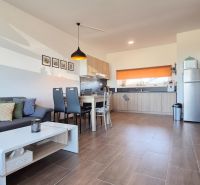 Wohnzimmer und Küche im Einfamilienhaus mit Holzboden und grauem Sofa.