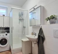 Badezimmer im Einfamilienhaus mit Waschmaschine, Duschkabine und weißem Waschbecken.