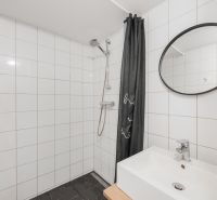 Badezimmer mit weißen Fliesen, Dusche und Waschbecken in einer 2-Zimmer-Wohnung.