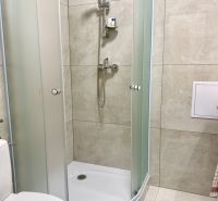 Duschkabine und Toilette im Badezimmer einer Einzimmerwohnung mit Fliesen.