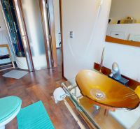 Badezimmer mit einem Waschbecken aus farbigem Glas, einer Dusche und einem Boden mit Holzdekor in einem Einfamilienhaus.
