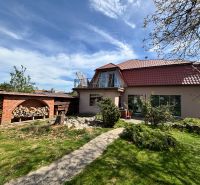 Ein Einfamilienhaus in Veľké Chlievany mit einem gepflegten Garten und einem Holzunterstand für Holz.