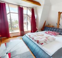 Schlafzimmer in einem Einfamilienhaus mit großen Fenstern und einem Boden in Holzoptik.