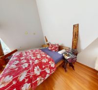 Ein Schlafzimmer im Dachgeschoss eines Einfamilienhauses mit Blumenbettwäsche und einem Boden in Holzoptik.