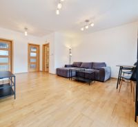 Ein Zimmer einer Dreizimmerwohnung mit einem Boden in Holzoptik, einem grauen Sofa und einem Tisch.