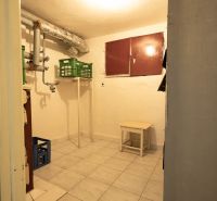 Praktischer Keller in einem Einfamilienhaus mit Fliesenboden, kleinen Möbeln und Rohrleitungen.