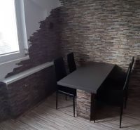 Essbereich mit Tisch und Stühlen in einer 2-Zimmer-Wohnung, Wand aus Stein.