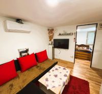Wohnzimmer mit Sofa, roten Kissen, Fernseher und Holzboden.