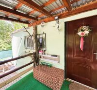 Eine Hütte in Gabčíkovo mit dekorativem Eingang, Geländer und Sitzbereich in der Nähe einer Grünfläche.