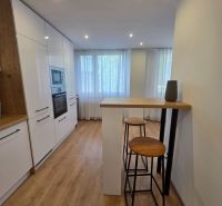 Küche mit weißen Schränken, Boden mit Holzdekor, hohe Stühle in einer 3-Zimmer-Wohnung.