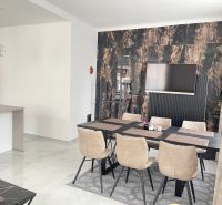 Esszimmer mit einem Tisch und sechs Stühlen, Holzboden, Fernseher an der Wand.