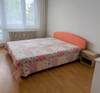 Schlafzimmer mit Bett und Patchwork-Überwurf in einer 2-Zimmer-Wohnung, Boden mit Holzdekor.