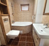 Badezimmer in einer 2-Zimmer-Wohnung mit Badewanne und Schränken, hellbraune Fliesen und Bodenfliesen.