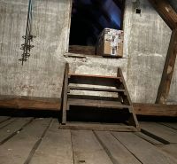 Der Dachboden des Einfamilienhauses mit einer Holztreppe und einem Paket.