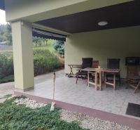 Die Terrasse des Einfamilienhauses in Trebostovo mit Holzgartenmöbeln und gepflegtem Grün.