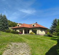 Ein Einfamilienhaus in Trebostovo mit einem roten Dach, umgeben von grünem Rasen und Bäumen.