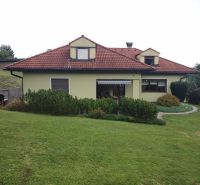 Ein Einfamilienhaus in Trebostovo mit rotem Dach, umgeben von grünem Rasen und Büschen.