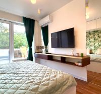 Schlafzimmer in einer 3-Zimmer-Wohnung mit großen Fenstern, grünen Vorhängen und einem Boden mit Holzdekor.