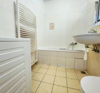 Badezimmer in einer 2-Zimmer-Wohnung mit Badewanne, Waschbecken und Waschmaschine, gefliest mit weißen Fliesen.