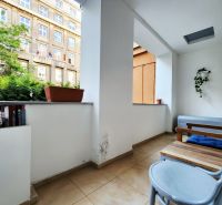 Ein Balkon in einer 2-Zimmer-Wohnung mit Blumentöpfen und Holzmöbeln.