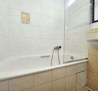 Badezimmer in einer 2-Zimmer-Wohnung mit Badewanne und Waschbecken, gefliest mit hellen Fliesen.